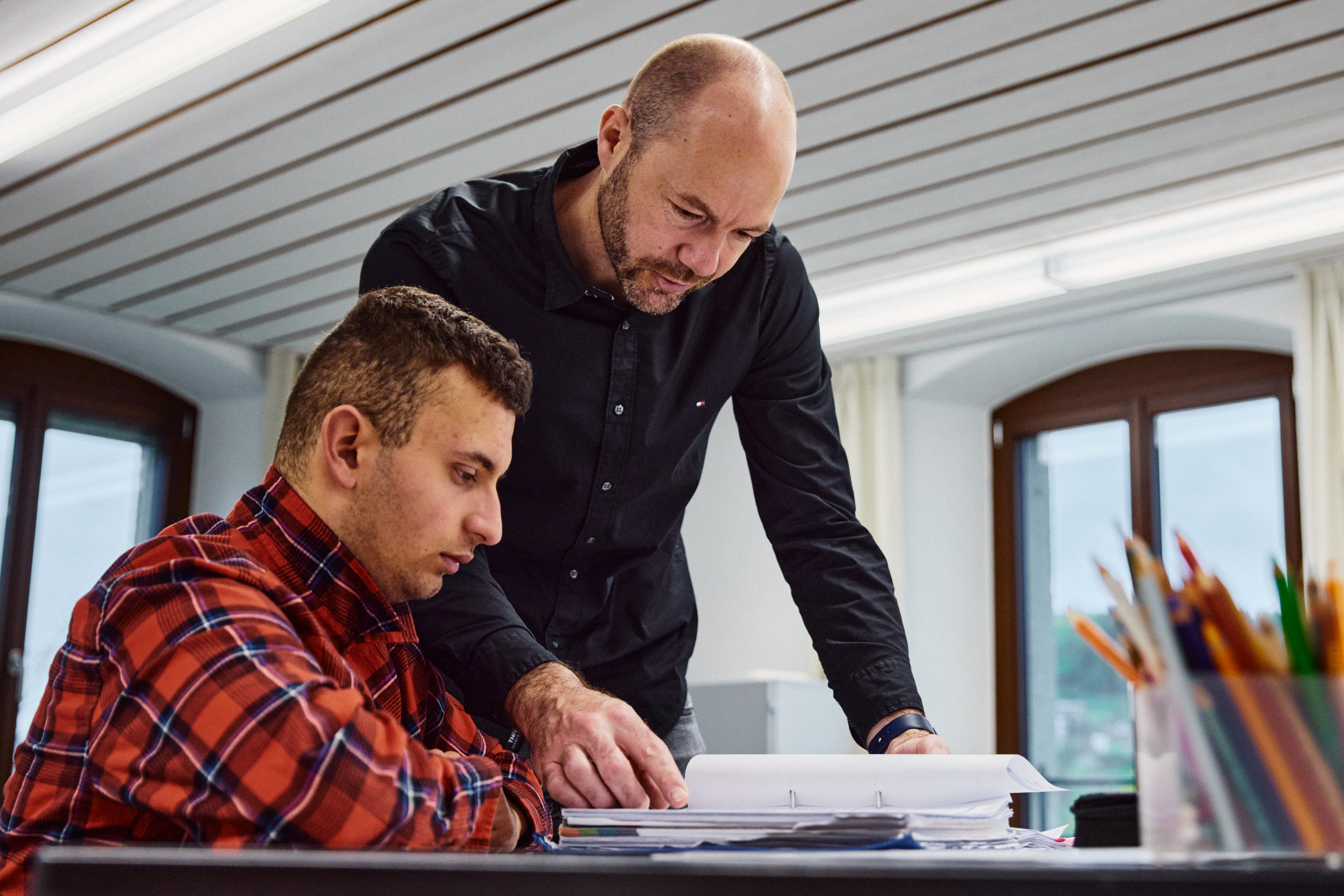 Lehrperson erklärt einem Schüler mit Unterstützungsbedarf Inhalte aus einem Ordner – individuelle Förderung im Fokus.