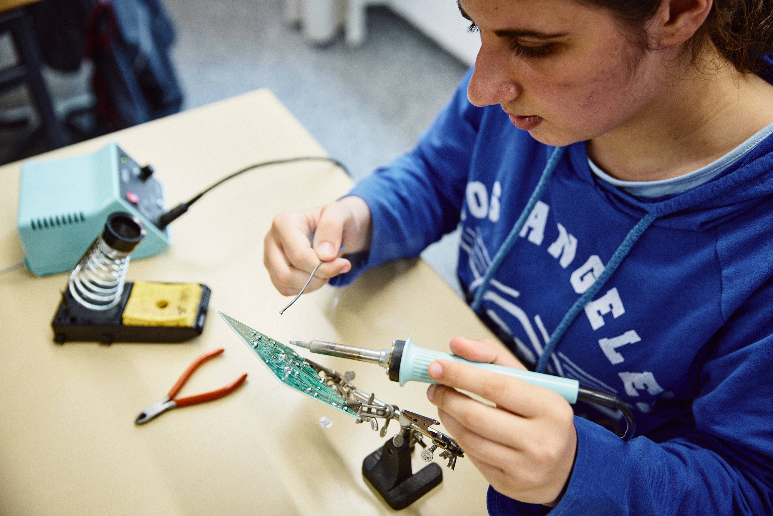 Eine Auszubildende führt konzentriert eine Lötarbeit am Tisch aus – Förderung berufspraktischer Kompetenzen